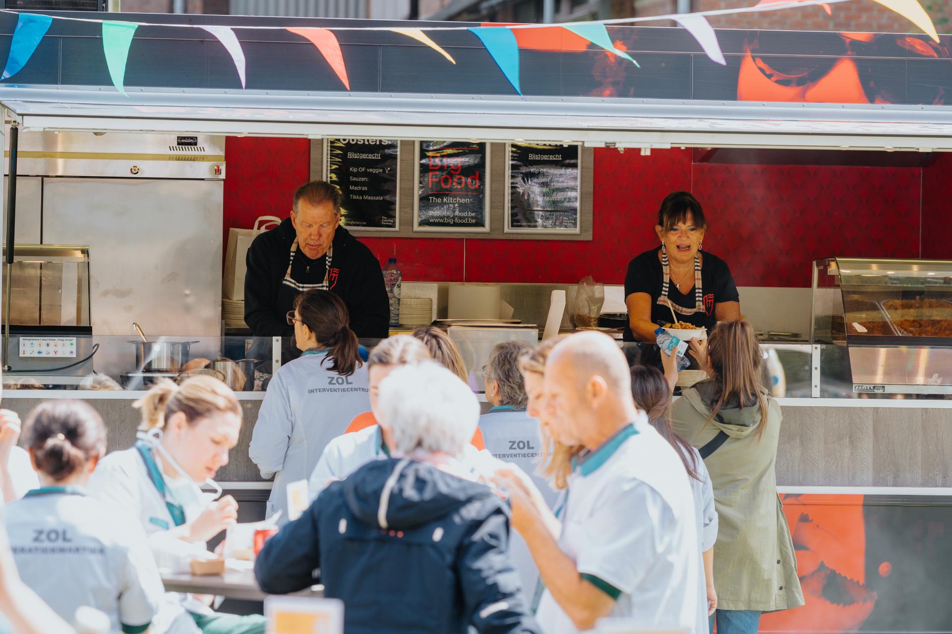 Medewerkers van De Snackcar bedienen gasten vanuit een mobiele frituur tijdens een groot evenement.